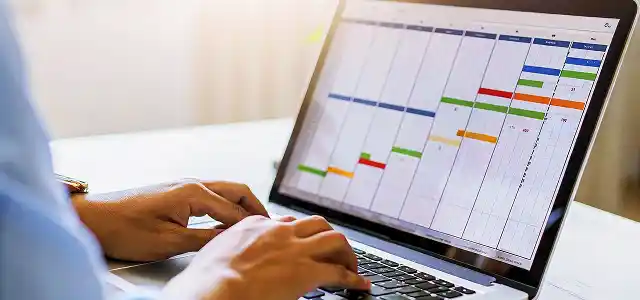 A person’s hands typing on a laptop displaying a colorful calendar or schedule.