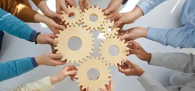 A group of hands working together to arrange wooden gears in a circular pattern.